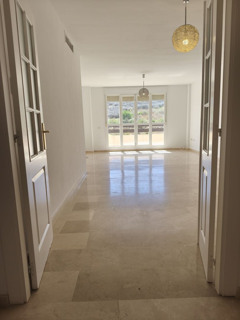 Spacious living room with marble floors, white walls, and large windows offering a scenic outdoor view.
