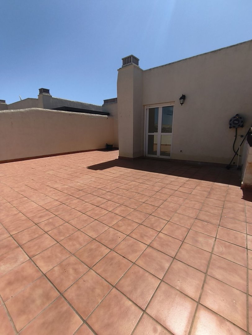 Terrace with terracotta tiles, glass door, and chimney under clear blue sky.
