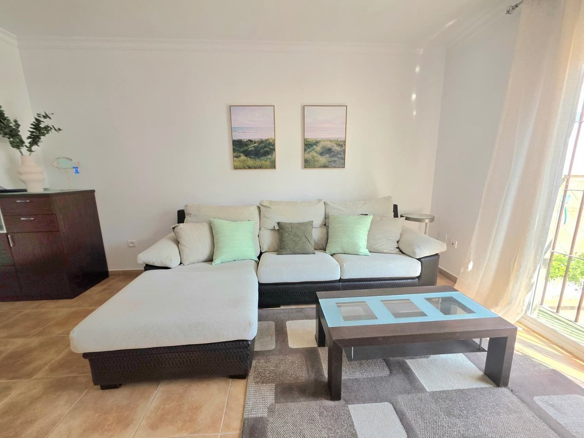 Modern living room with white sofa, glass coffee table, and beach-themed wall art.
