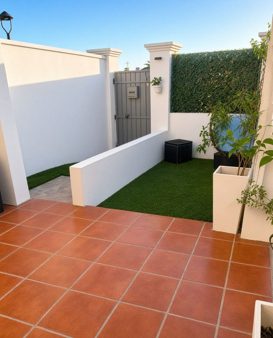 A paved terrace leads to a private garden area with artificial lawn, a gate, and potted plants.