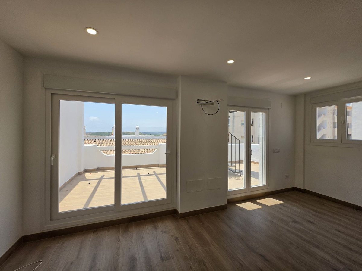 A spacious room with large sliding glass doors opening to a terrace with a view of tiled roofs and the distant horizon.