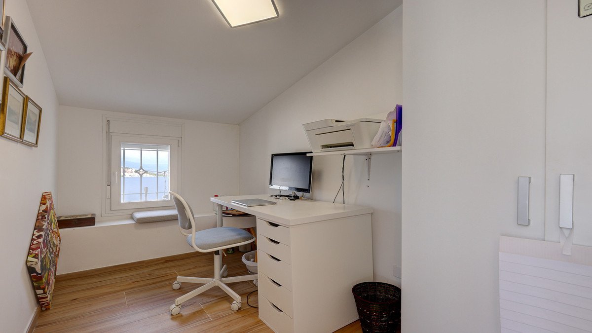 A white home office with a desk, computer, printer, and a window offering a view of the sea.