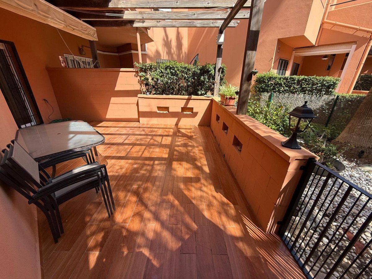 Sunlit terrace with wooden table and chairs, surrounded by orange walls and greenery