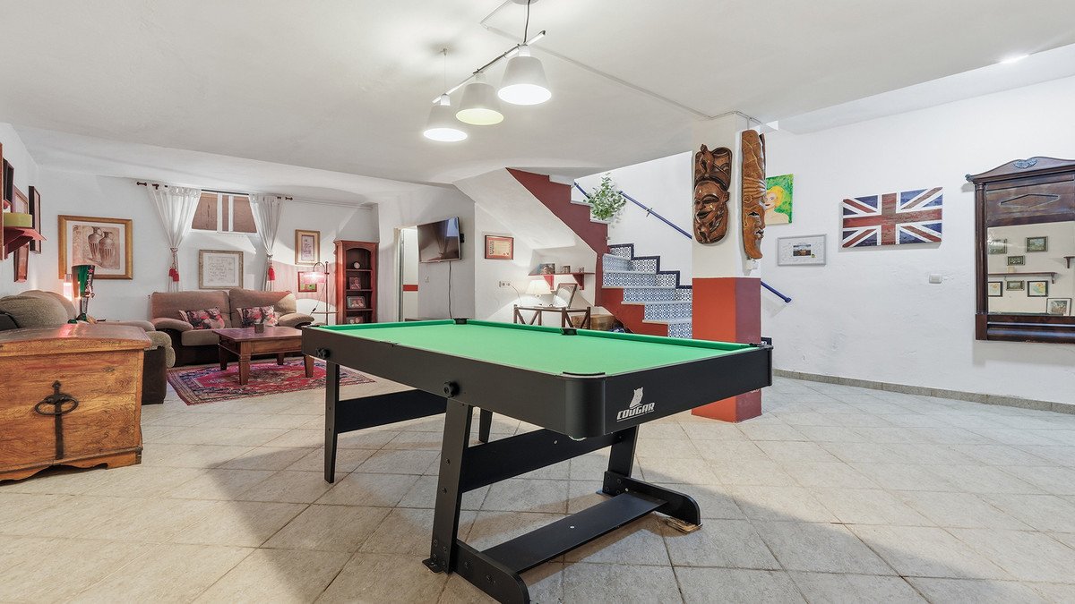 A spacious living room with a pool table, staircase, and eclectic decor including a British flag and tribal masks.