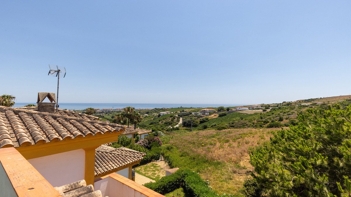 Terrace view from a villa overlooking the sea, hills, and greenery under a clear blue sky.