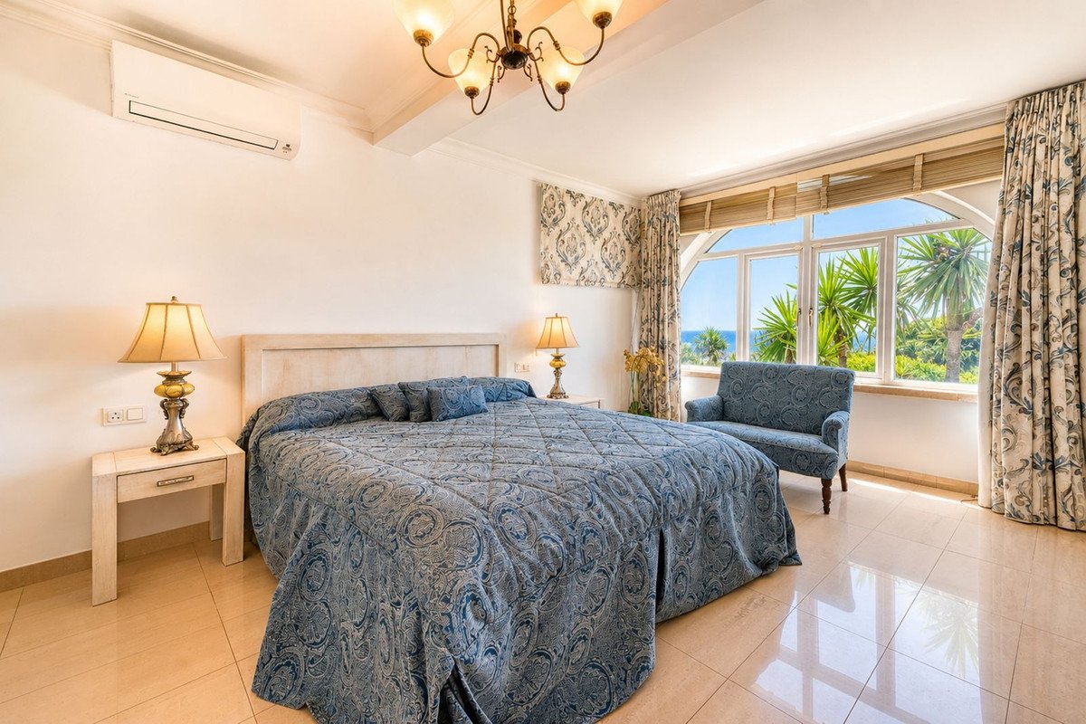 Elegant bedroom with large bed, matching armchair, and scenic ocean view