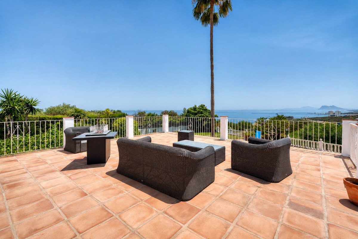 Terrace with wicker furniture, fire pit, and ocean view under palm tree.