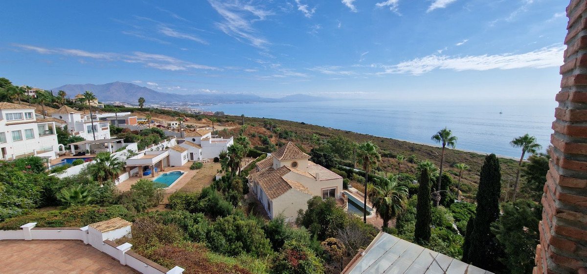 A scenic view of coastal villas with pools and the sea, overlooking mountains under a blue sky.