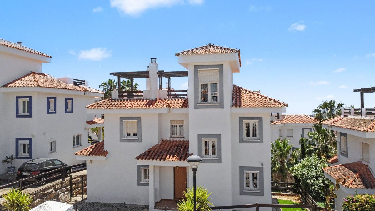 White villa with terracotta roof, blue window frames, and palm trees under a clear blue sky.
