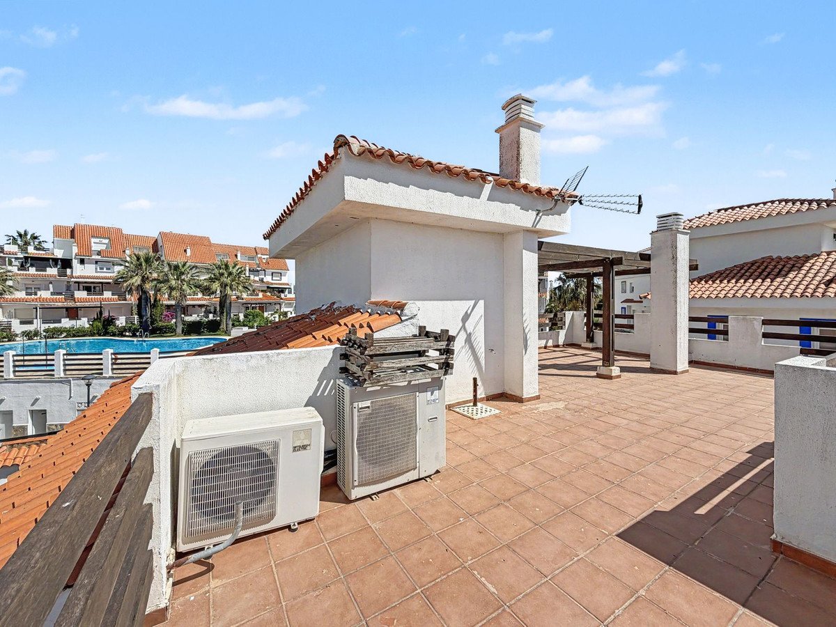 Rooftop terrace with tiled floor, air conditioning units, and a view of a pool and surrounding buildings under a clear blue sky.