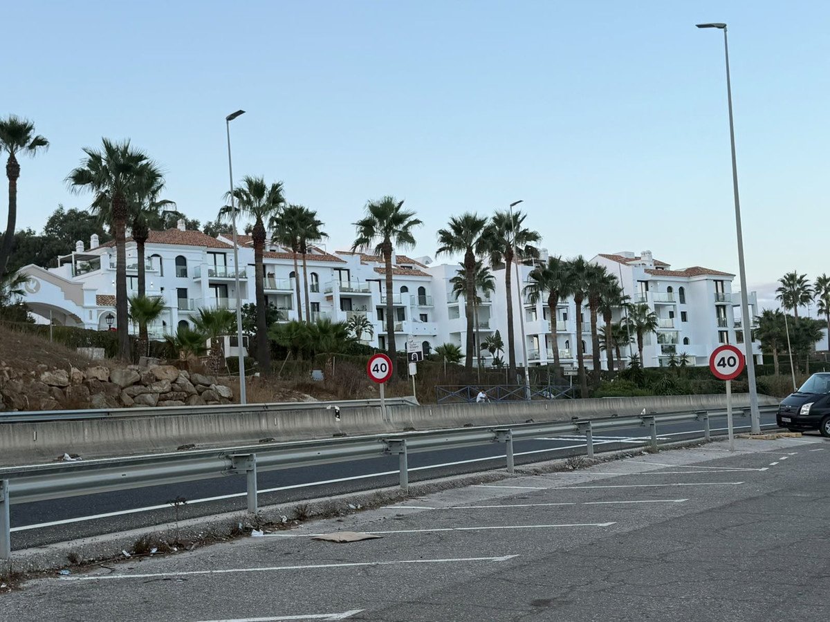 White apartment buildings with balconies and palm trees, overlooking a road with speed limit signs.