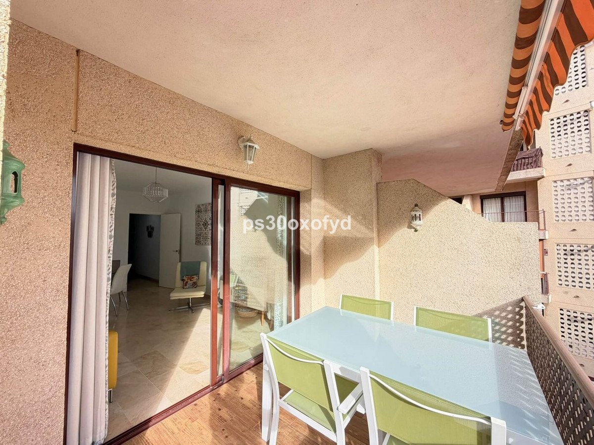 Balcony with glass dining table and green chairs, sliding doors to interior.