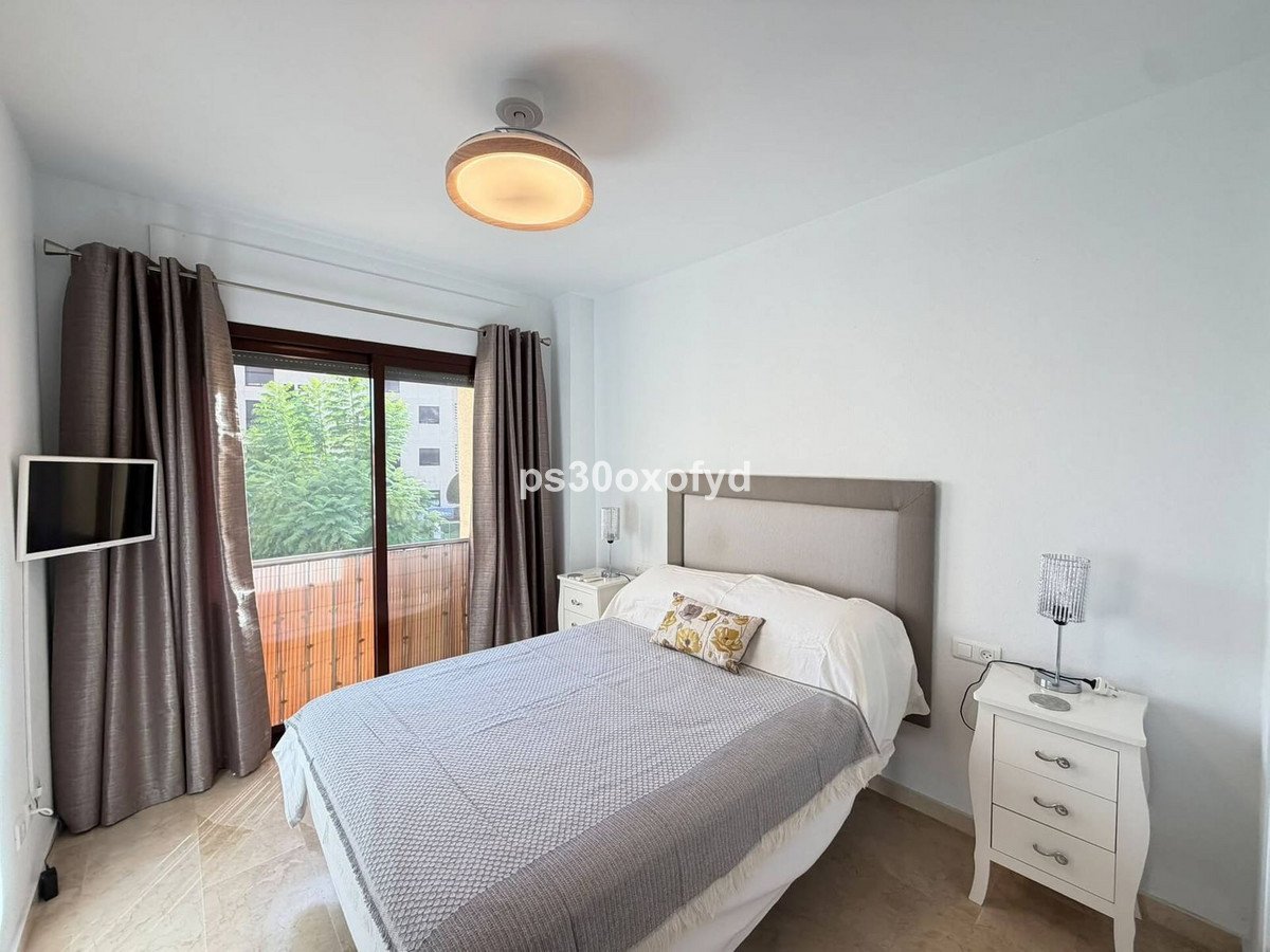 A bright bedroom with a double bed, white nightstands, and a balcony view through sliding doors.