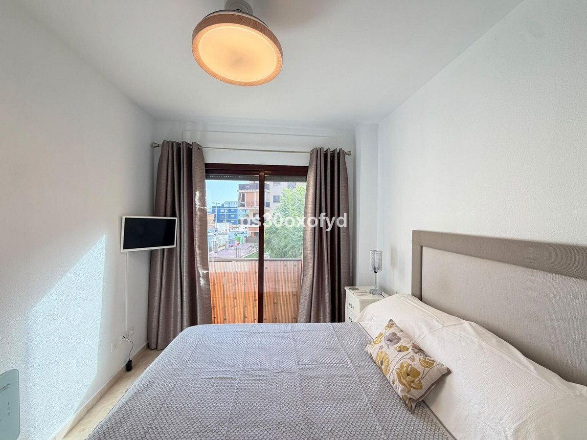 A bright bedroom with a double bed, sliding glass doors to a balcony, and a wall-mounted TV.