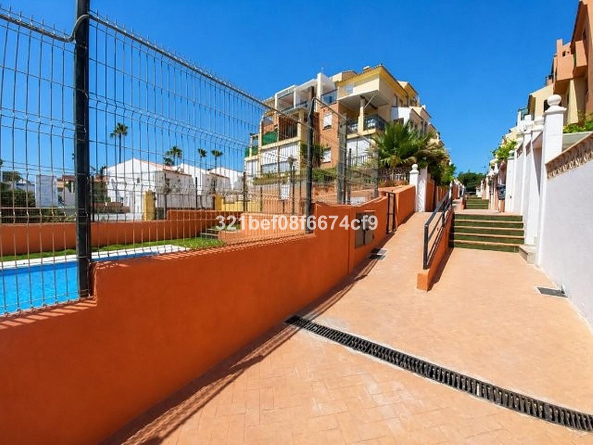 A pathway leads past a swimming pool and towards apartment buildings under a clear blue sky.
