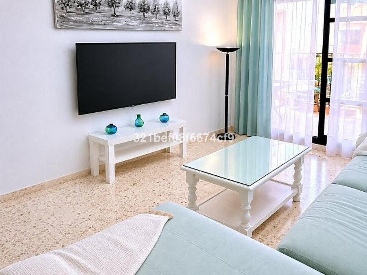 A modern living room features a wall-mounted TV, a white coffee table with a glass top, and bright curtains leading to a balcony.
