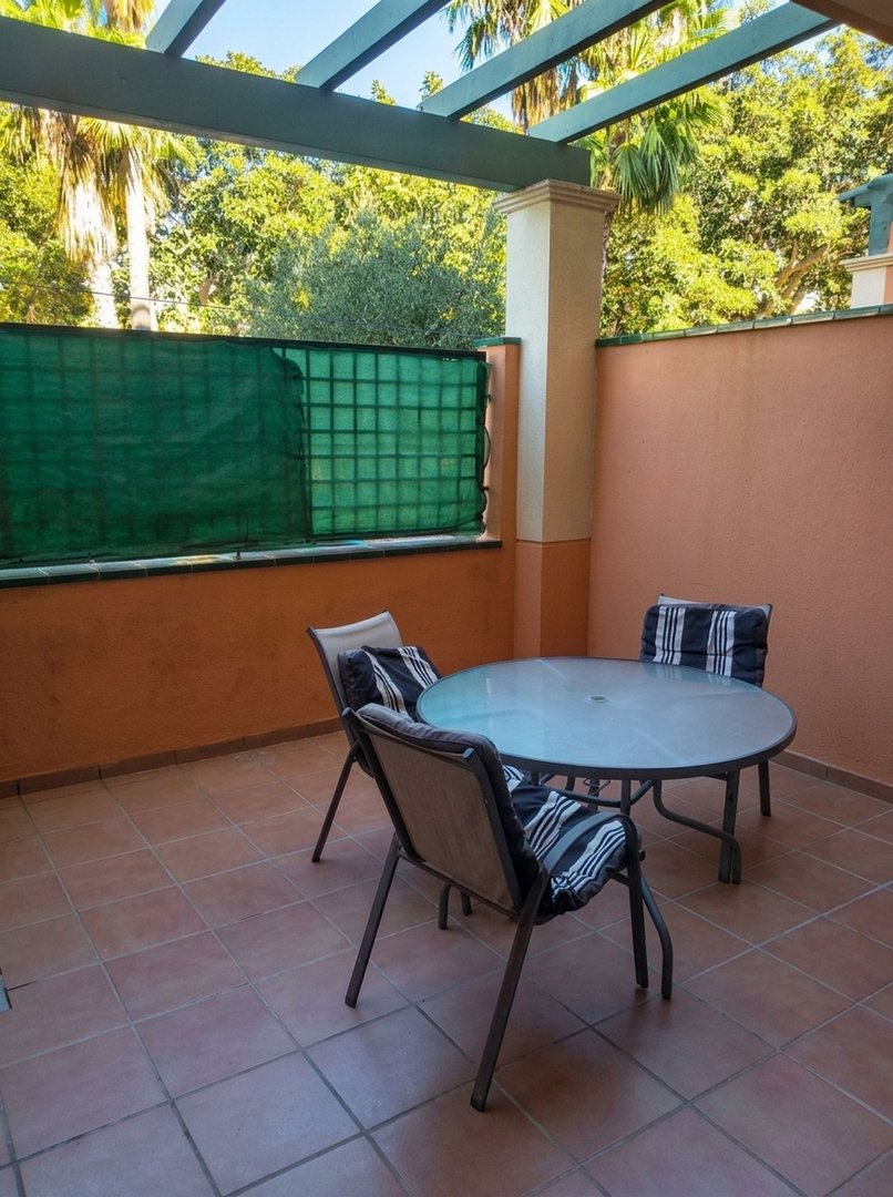 Terrace with a round glass dining table and chairs, overlooking palm trees and lush greenery.