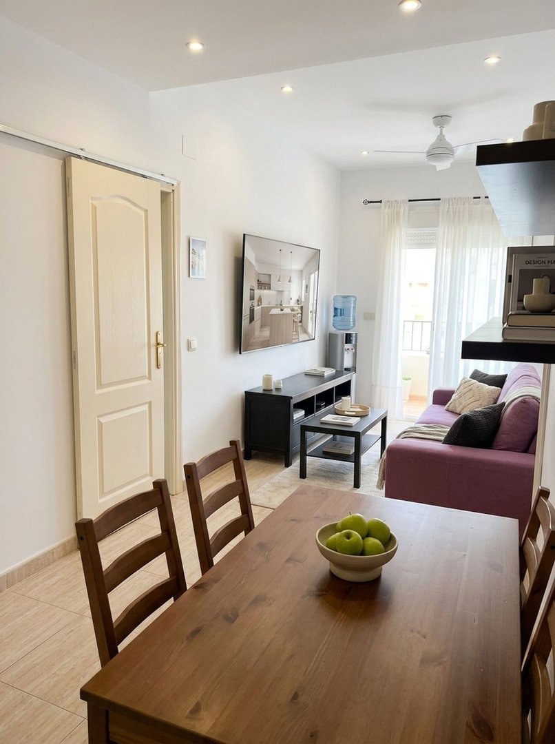 Modern living and dining area featuring a purple sofa, coffee table, TV, and a wooden dining set with a balcony visible in the background.