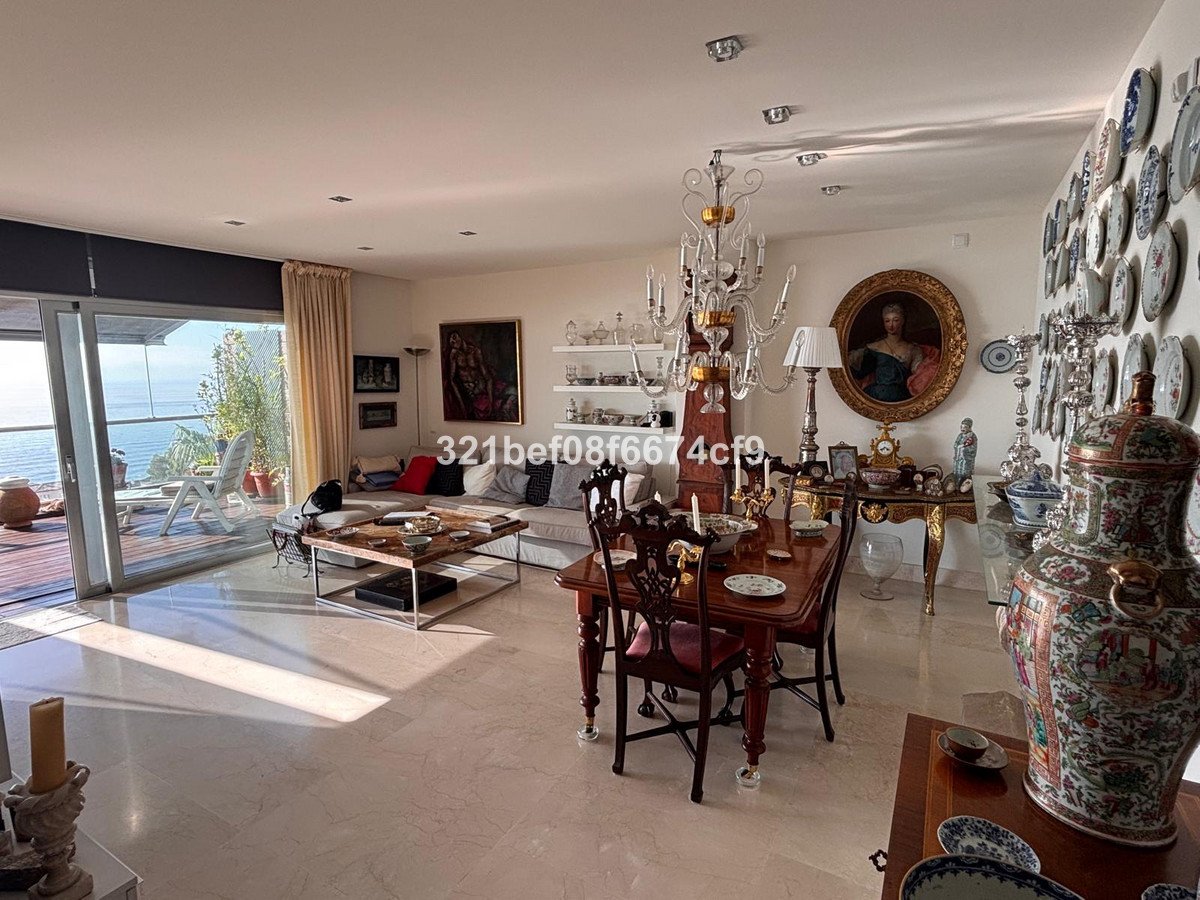 Elegant living and dining room with sea view, balcony access, crystal chandelier, and ornate decor.