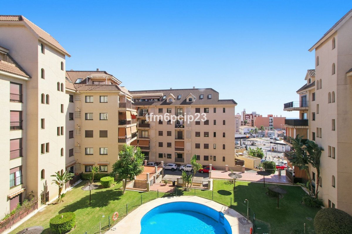 Exterior view of a modern apartment complex with balconies, a swimming pool, and a well-maintained garden on a sunny day.