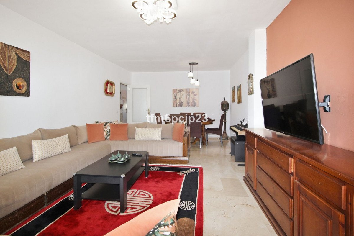 A spacious living and dining area with a sectional sofa, coffee table, dining table, and a wall-mounted TV.
