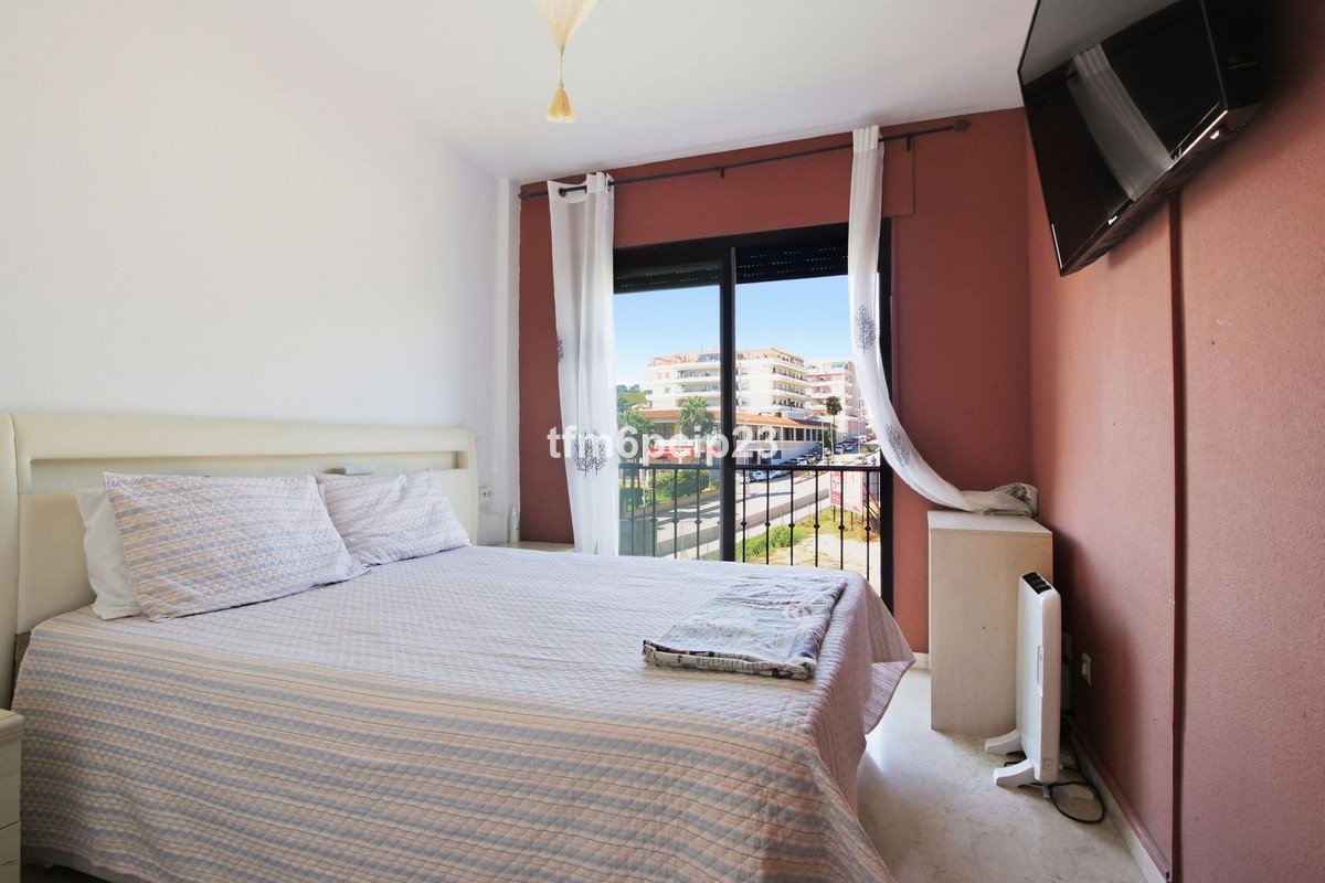 A bedroom with a bed, a TV on the wall, and a balcony with a view of buildings and trees.