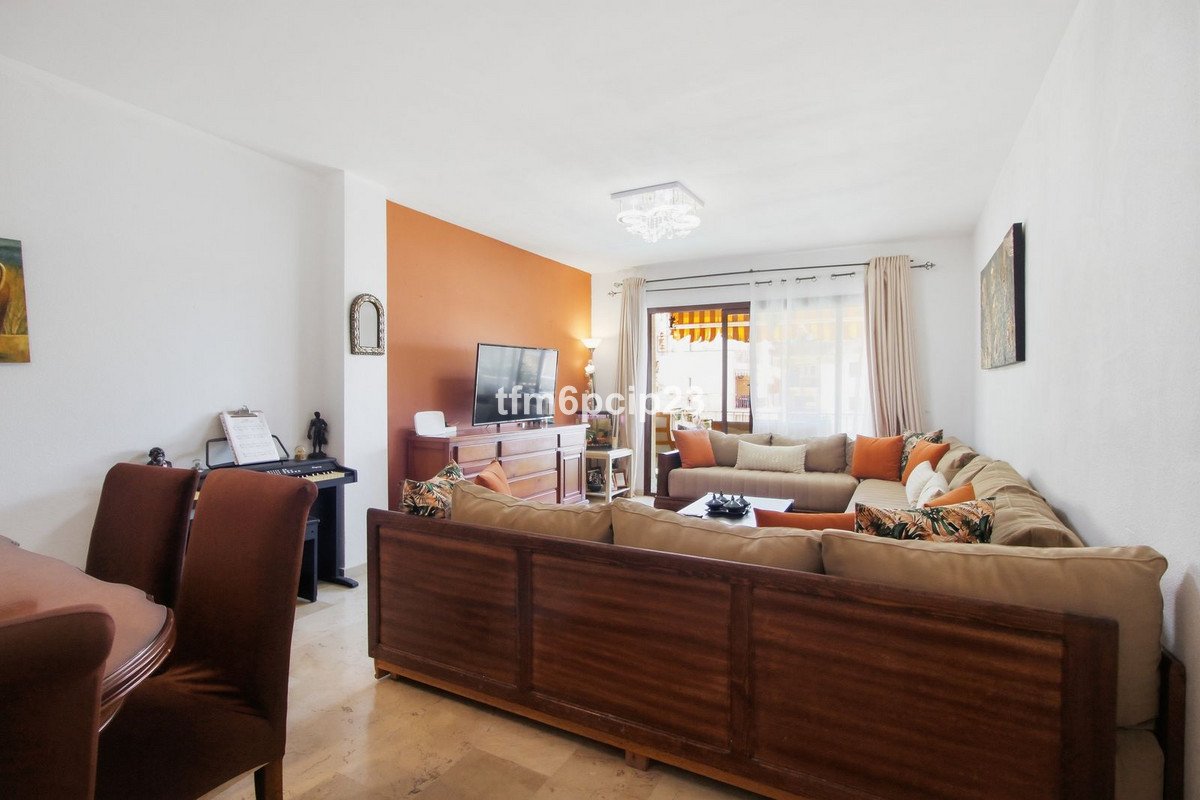 A spacious living room with a large sectional sofa, a media unit with a TV, and a dining area with chairs and a keyboard.