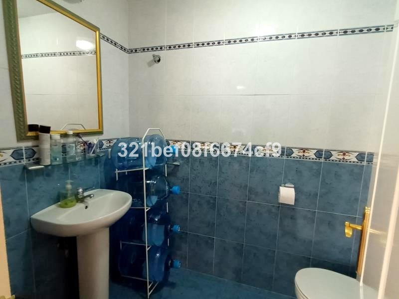 A small bathroom with a sink, toilet, large mirror, and a rack of water bottles.