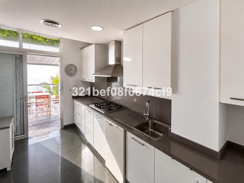 Modern white kitchen with stainless steel appliances, overlooking a balcony with ocean views and outdoor dining.