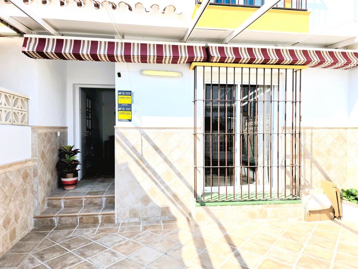 Exterior view of a house entrance with a striped awning, tiled patio, and barred windows.