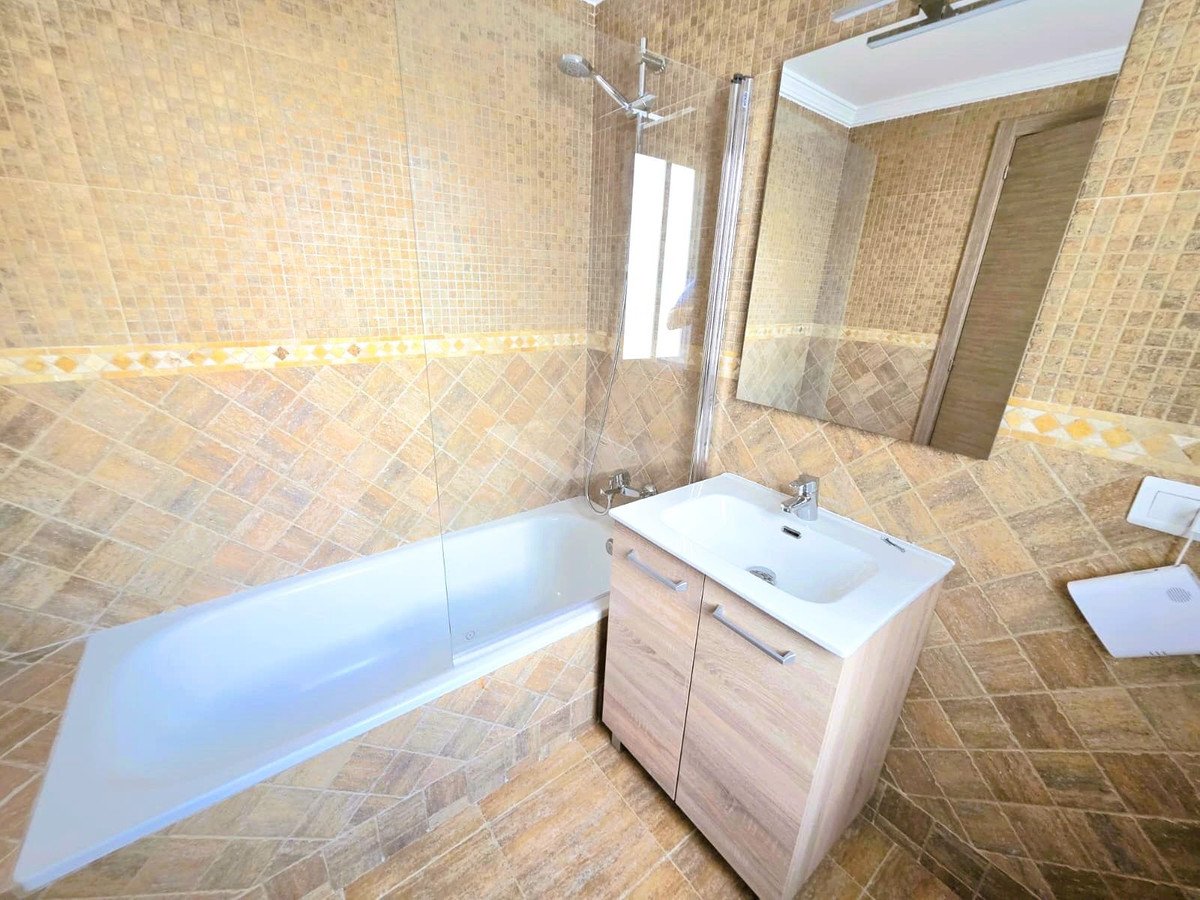 A modern bathroom with a tiled shower and bathtub, a vanity with sink, and a large mirror reflecting the room.