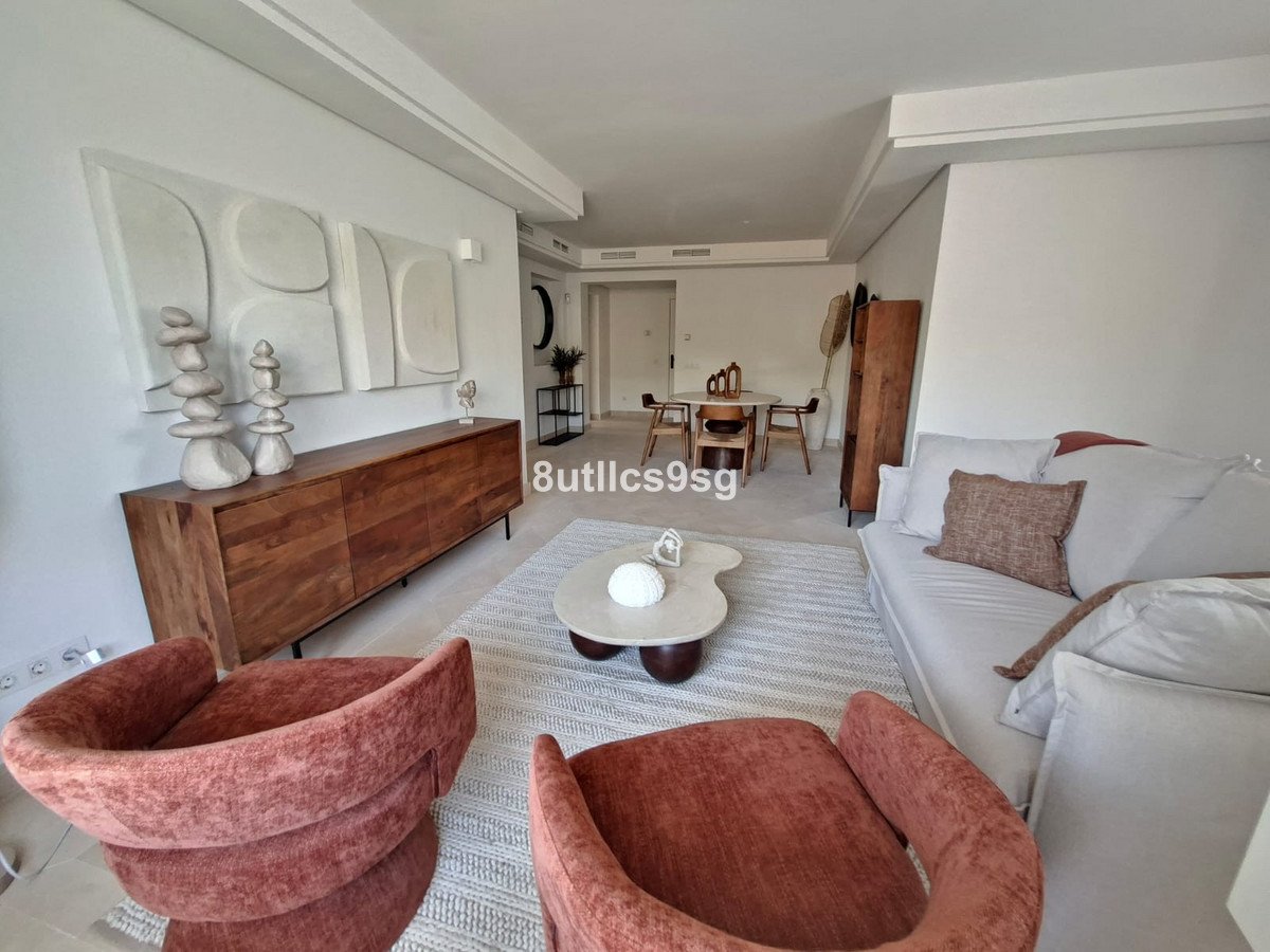 Modern living room with white sofa, pink armchairs, wooden console, and abstract wall art.