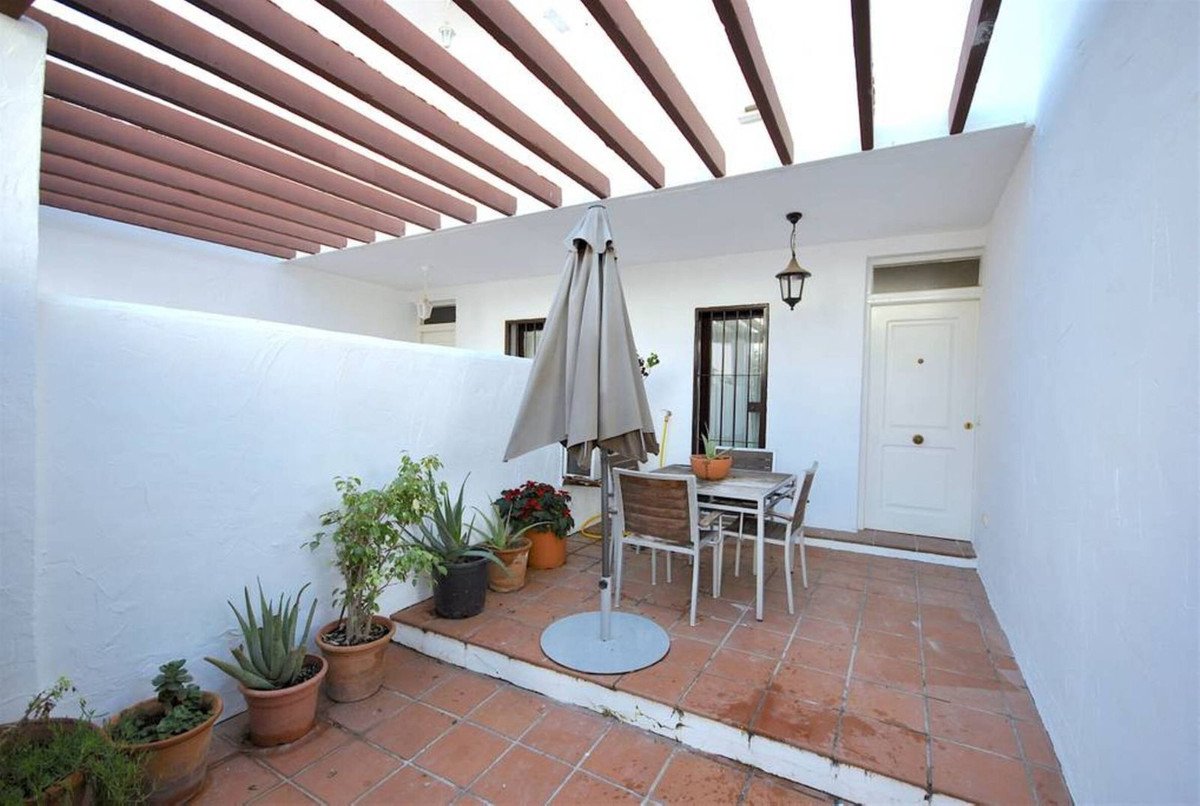 Covered patio with terracotta tiles, white walls, wooden pergola, table, chairs, and potted plants.