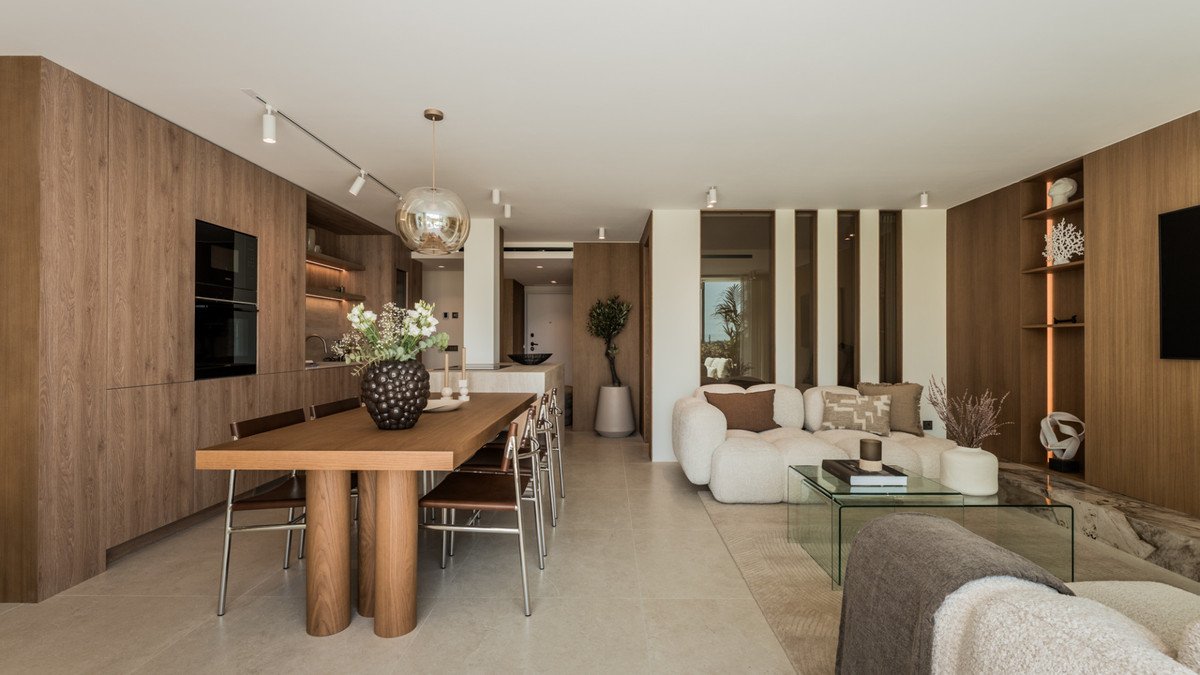 Modern open-plan living and dining area with wooden accents, glass table, and cozy seating.