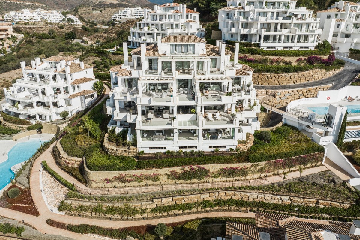 Aerial view of a modern white villa with terraces, pools, and lush gardens on a hillside.