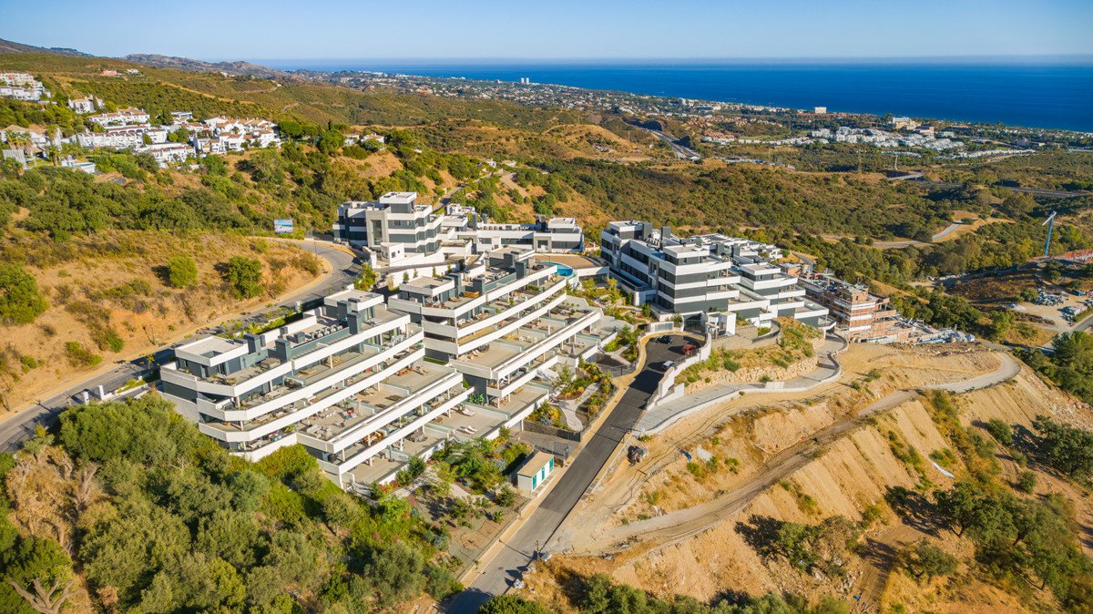 Aerial view of modern multi-story apartments with balconies on a hillside overlooking the sea and coastline.