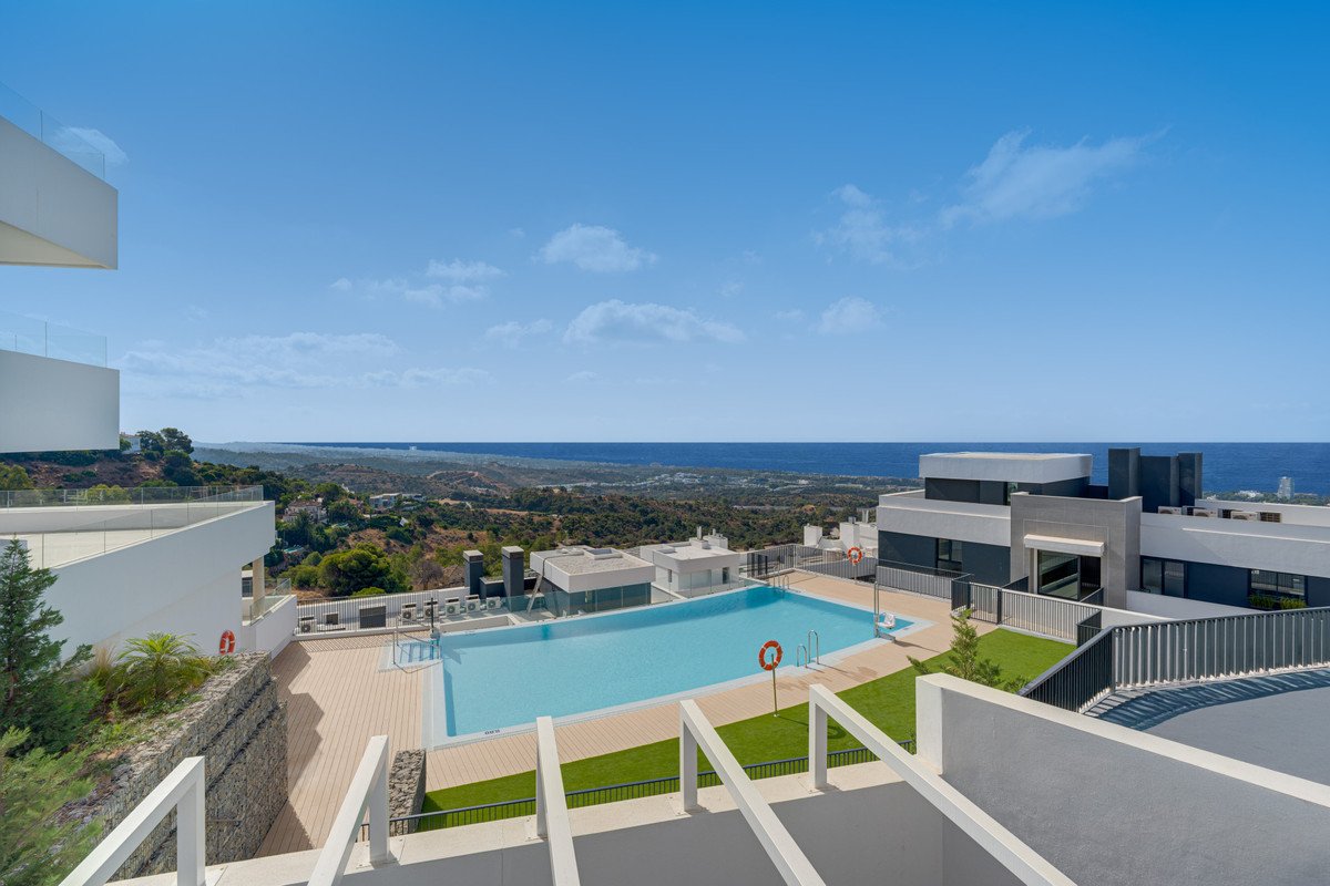 Modern apartment complex with a large swimming pool and terrace offering panoramic views of the sea and surrounding landscape.