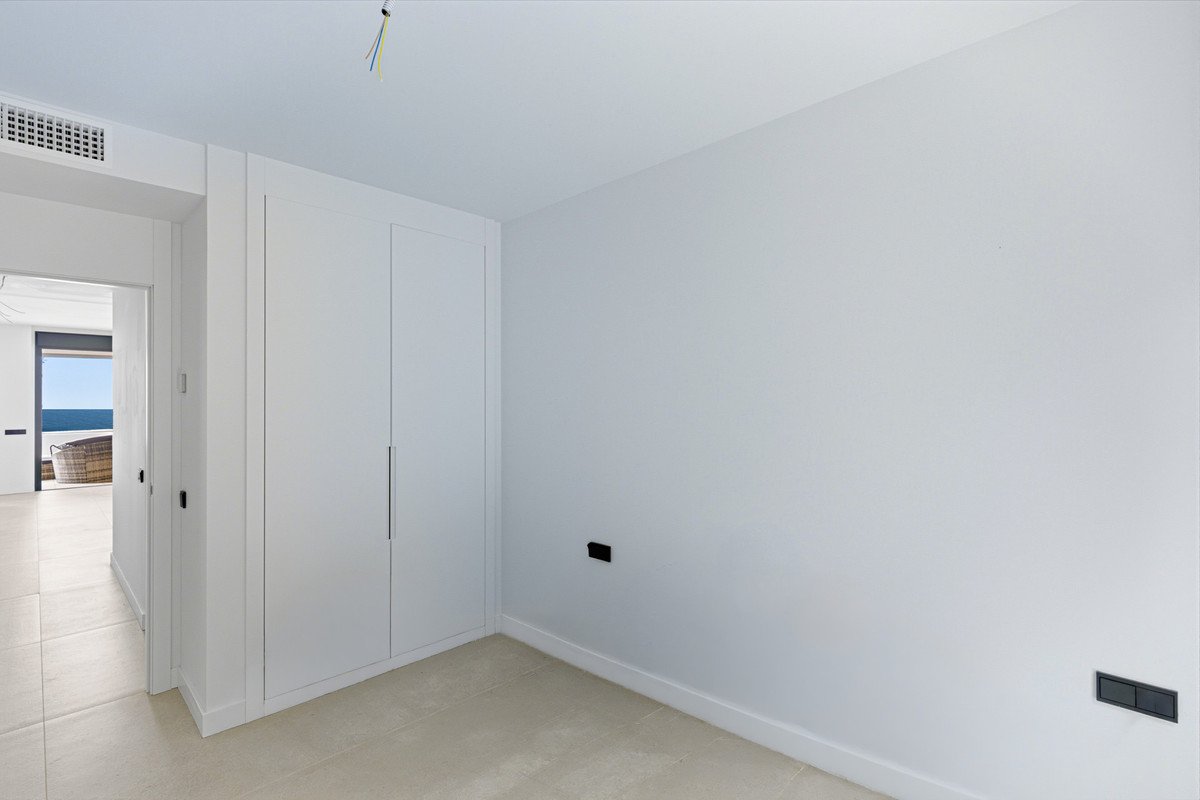 Modern bedroom with built-in wardrobe and a glimpse of the sea through an open doorway.