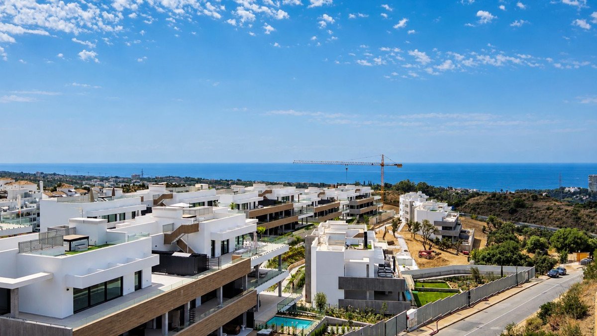 Modern apartment buildings with balconies and terraces overlooking the blue sea on a sunny day.