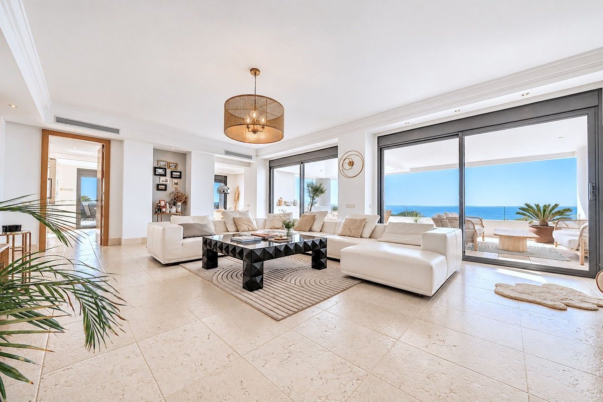 Modern living room with white sofas, black coffee table, and ocean view through large sliding doors