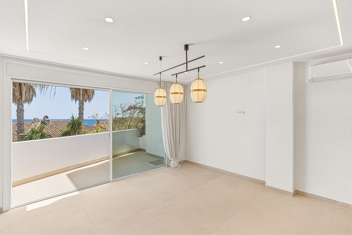Interior living room with sliding glass doors opening to a balcony with palm trees and a sea view.