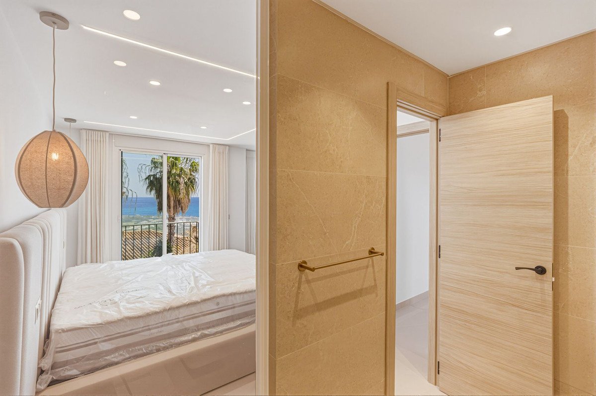 Bedroom with a large bed, featuring sliding glass doors that open to a balcony with a sea view and palm trees.