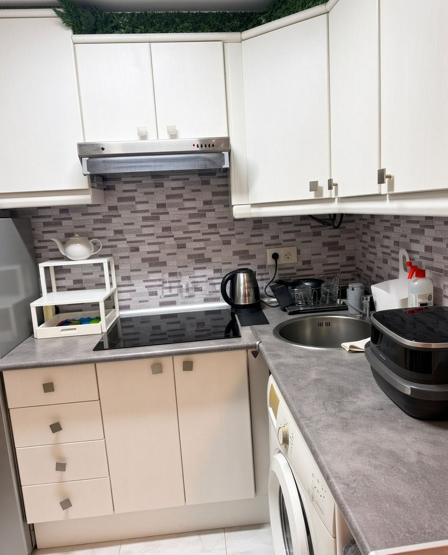 A modern kitchen with white cabinets, a grey speckled backsplash, induction hob, sink, and washing machine.
