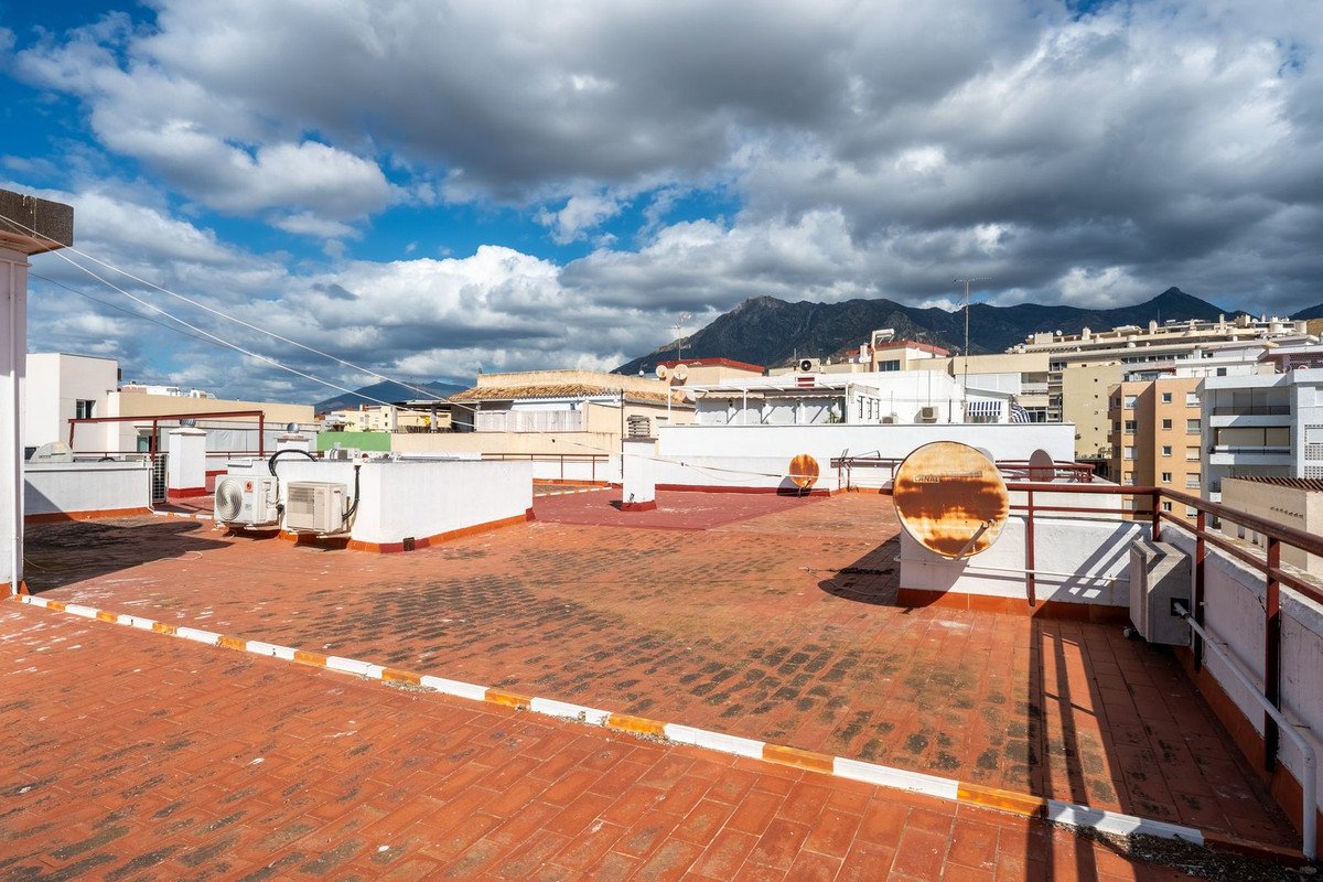 Expansive tiled terrace with air conditioning units, overlooking buildings and distant mountains under a cloudy sky.