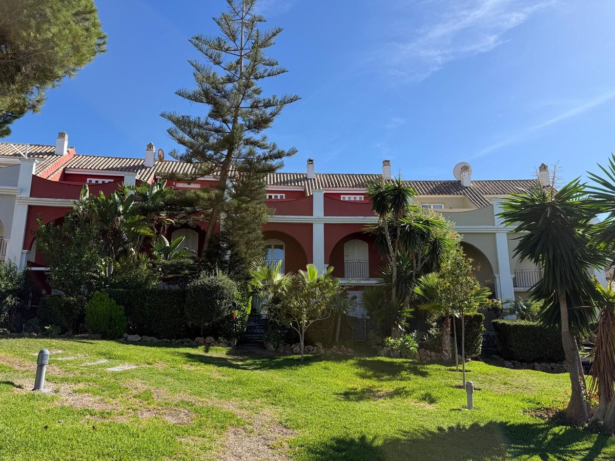 Red townhouse with garden and palm trees under blue sky