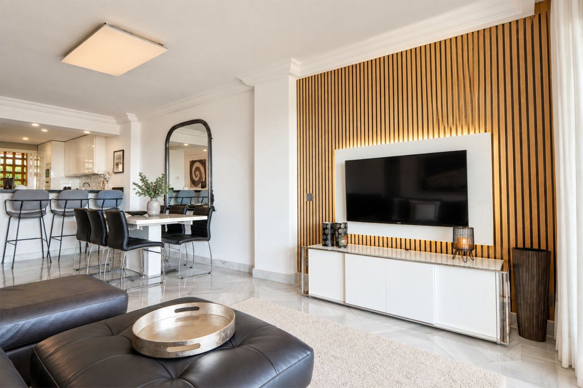 Modern living room with open plan kitchen, black leather seating, and wooden accent wall.