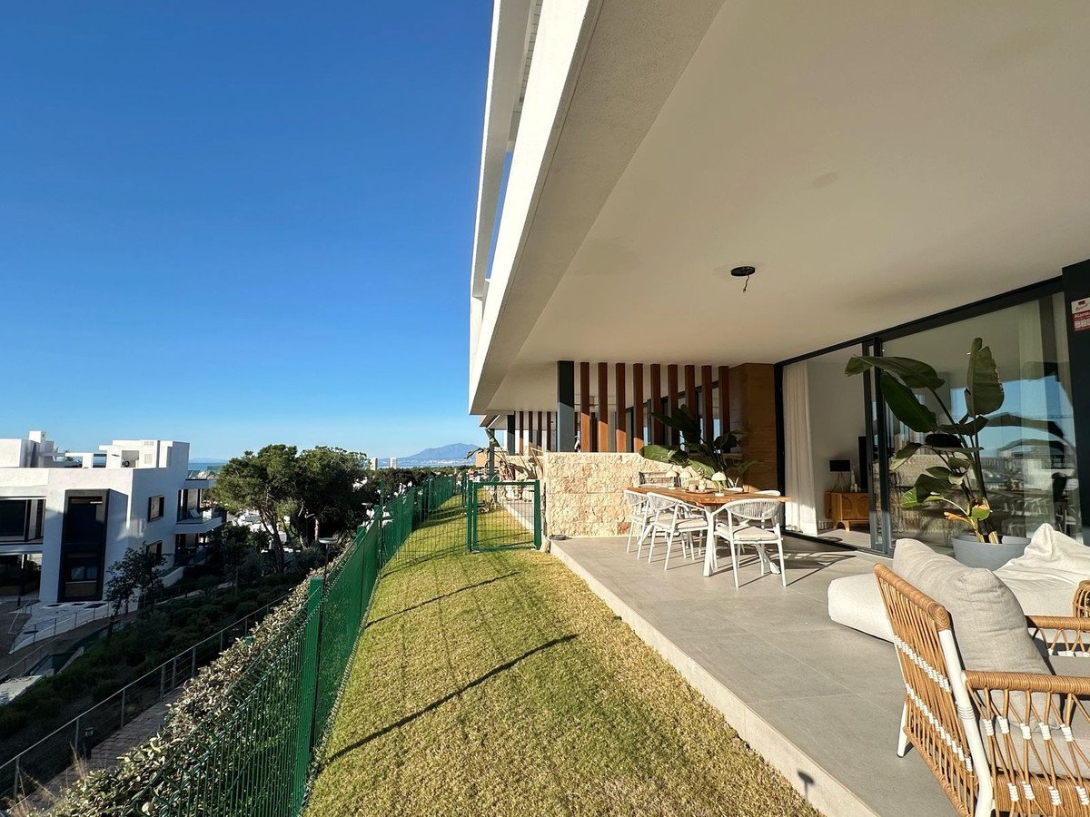 Modern terrace with dining table and lounge area, offering a serene view of the sea and surrounding landscape under a clear blue sky.