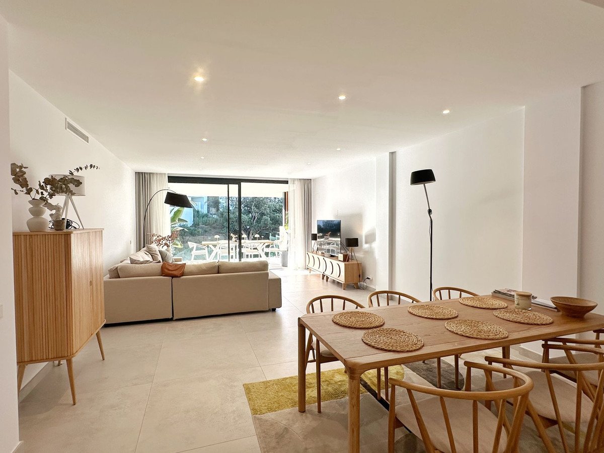 Modern living and dining area with a sectional sofa, wooden table, and large sliding doors leading to an outdoor patio with a view.