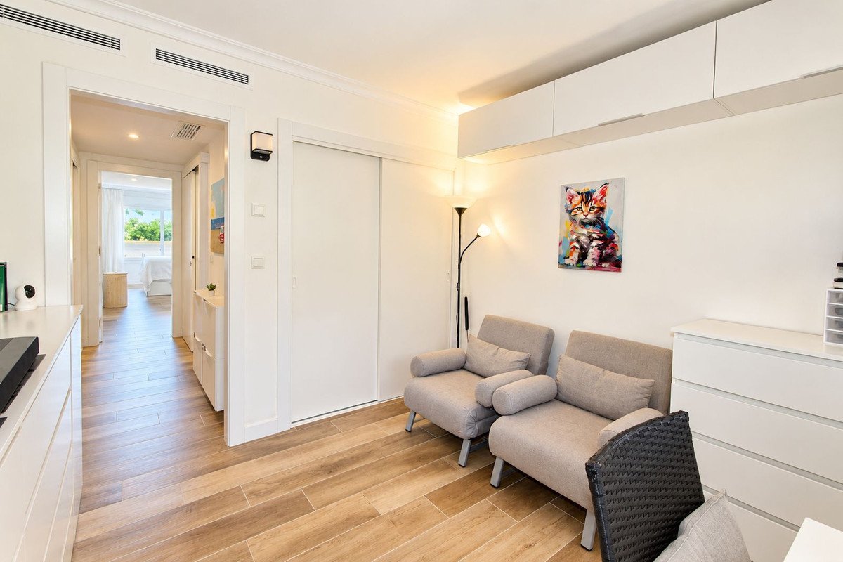 A bright hallway leads to a bedroom, with a seating area featuring two armchairs, a floor lamp, and colorful cat art on the wall.