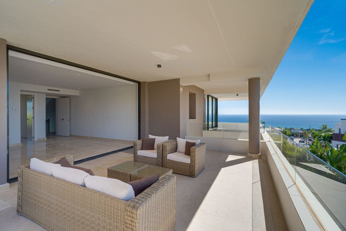 Spacious terrace with wicker furniture and a stunning panoramic sea view, overlooking a coastal town.